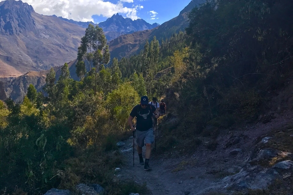 A hiker on a rocky trail surrounded by mountains and trees.