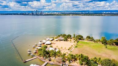 A coastal cityscape with a beach area featuring umbrellas and palm trees.