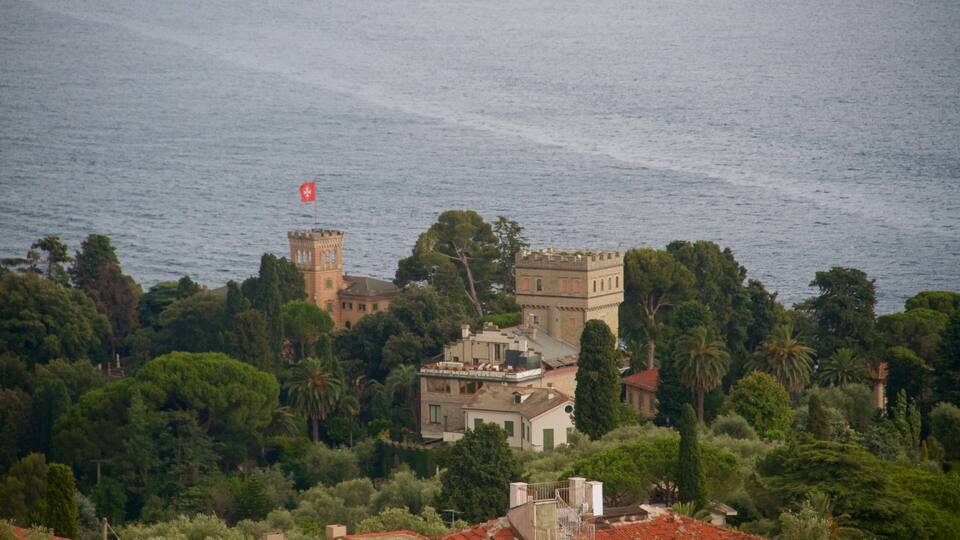 A coastal town with a prominent tower and castle-like building surrounded by lush greenery and the sea.