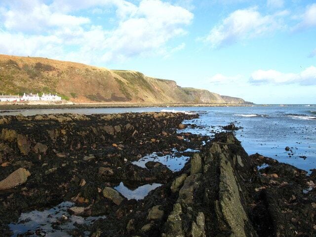 A rocky coastline with cliffs and a small settlement in the distance.