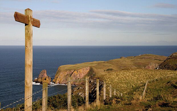 A wooden cross sign, grassy hills, and the ocean.