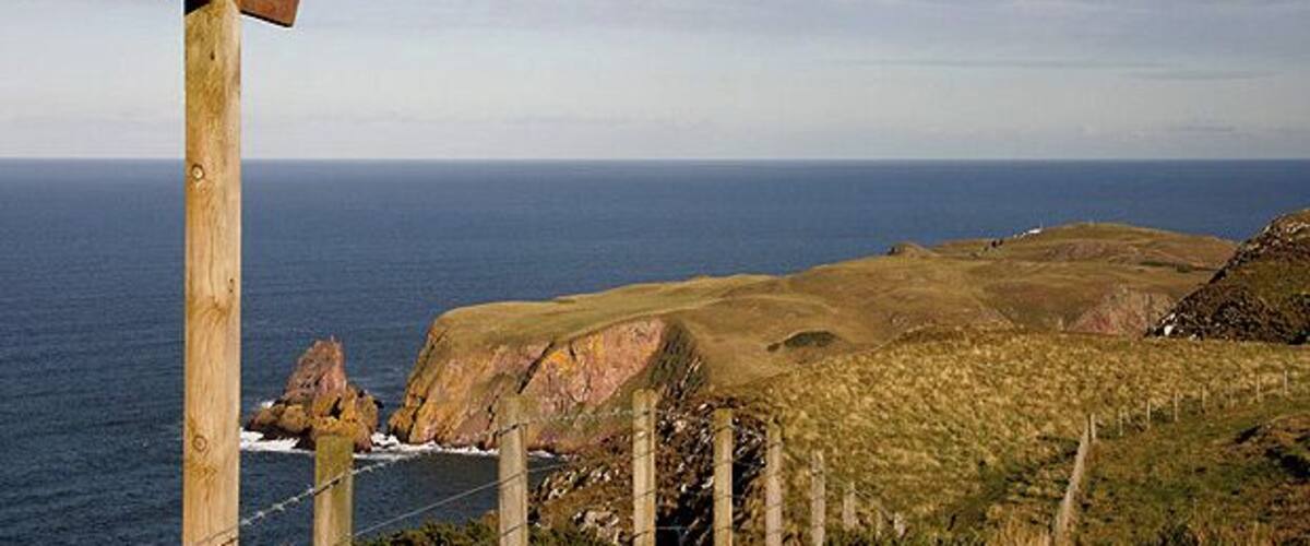 A wooden cross sign, grassy hills, and the ocean.