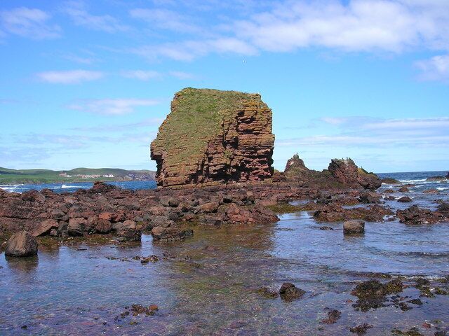 A rocky coastal landscape with a prominent rock formation and clear blue sky.