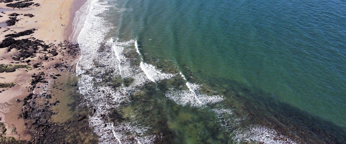 A coastal beach with clear waters, a sandy shore, and rocky areas.