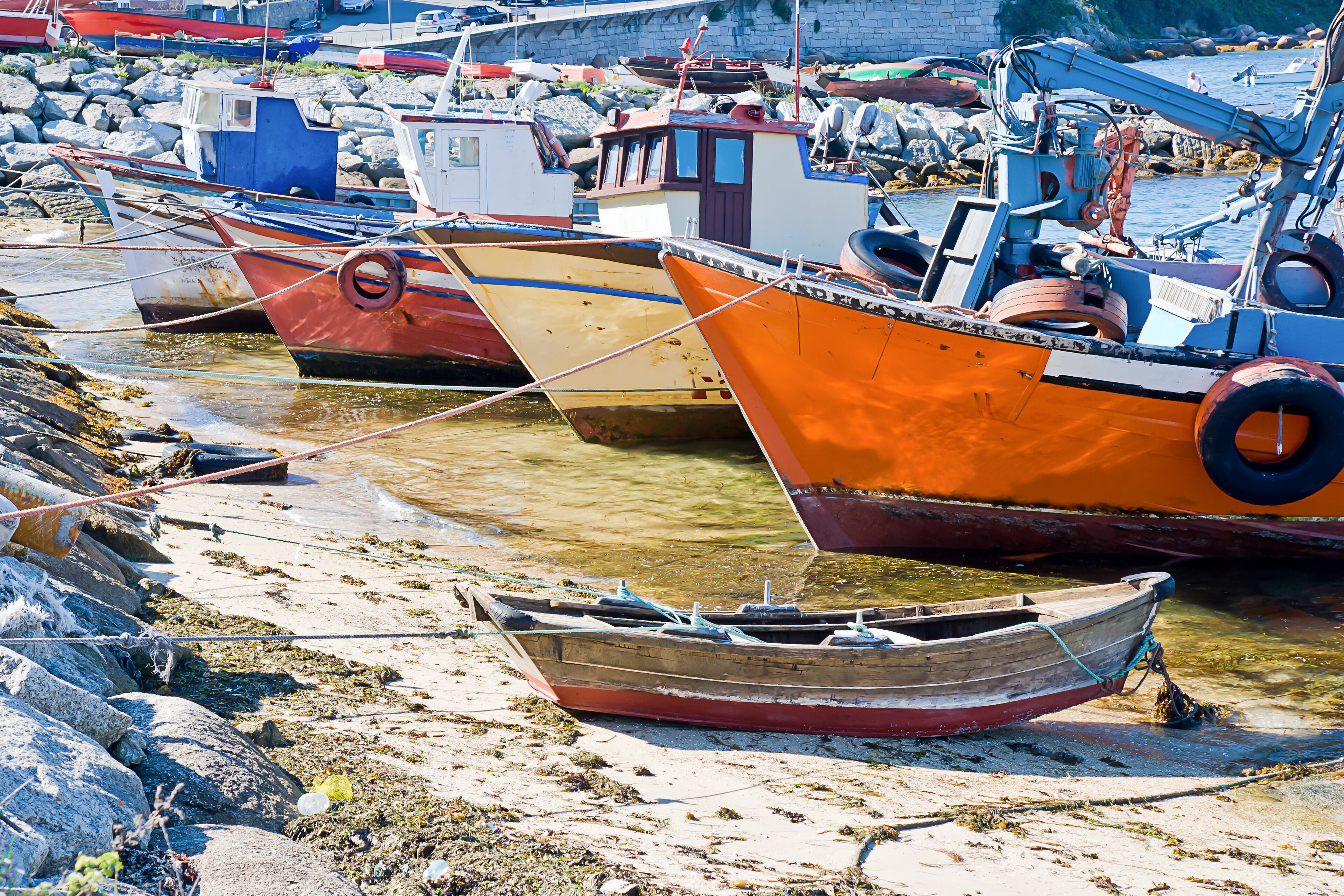 A harbor with several boats tied to the shore, surrounded by rocks and debris.