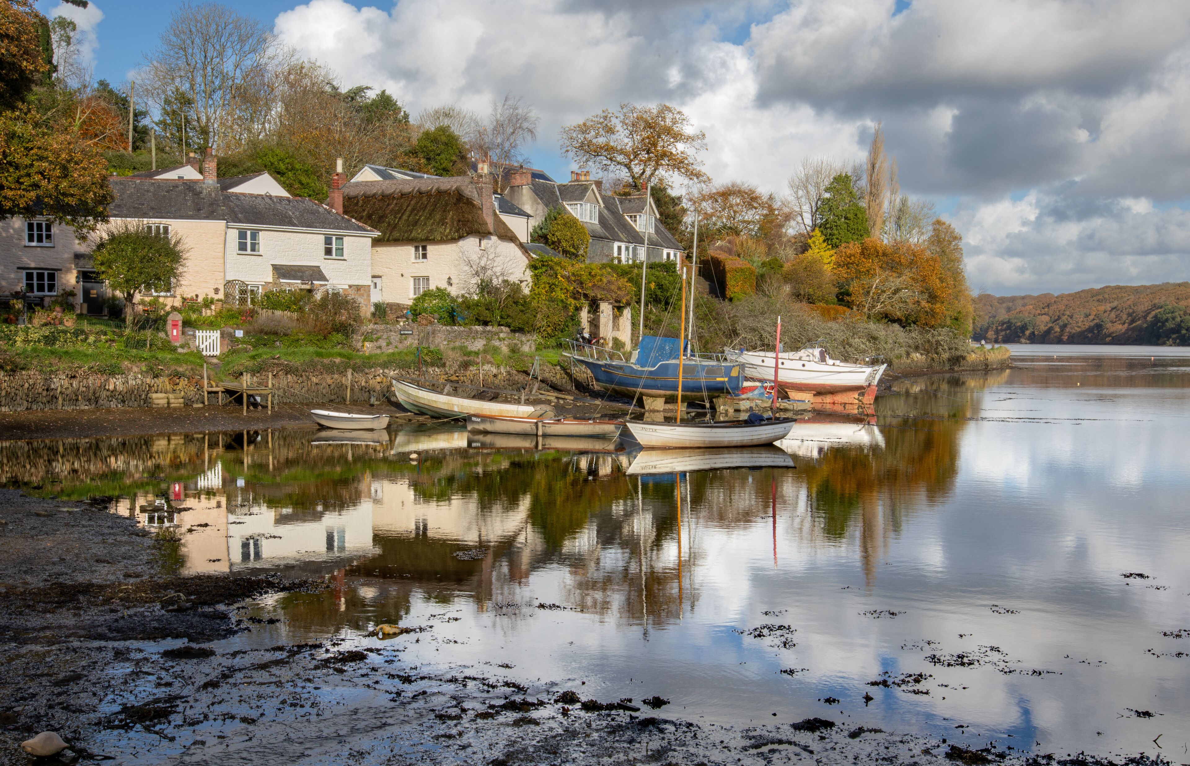 A calm river with boats docked, houses, and autumn trees along the shore.