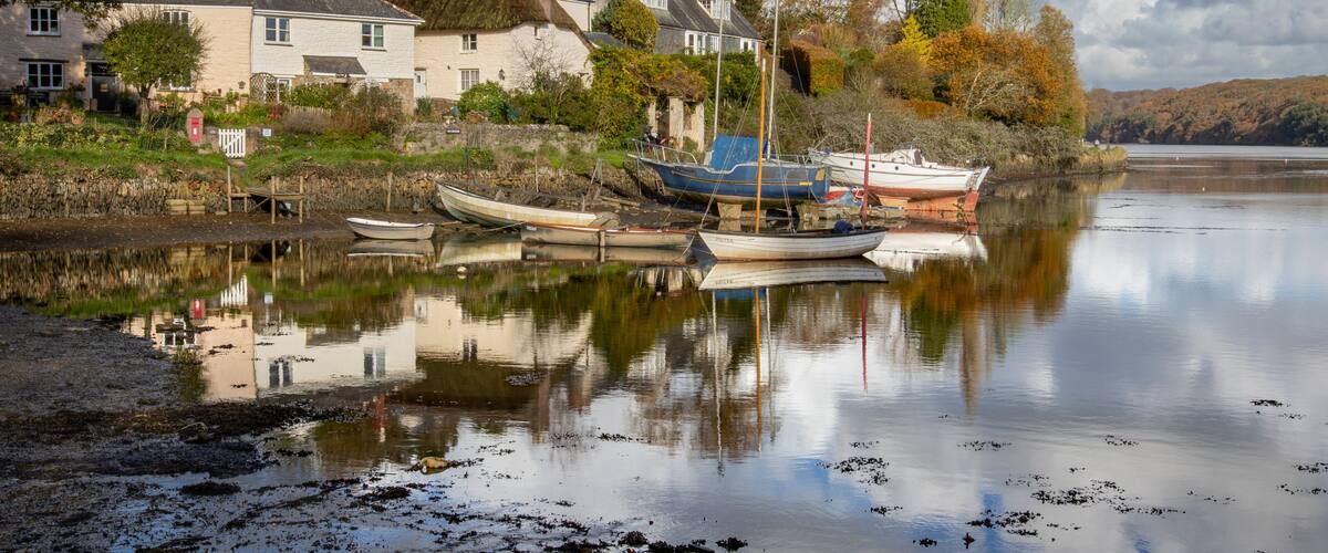 A calm river with boats docked, houses, and autumn trees along the shore.