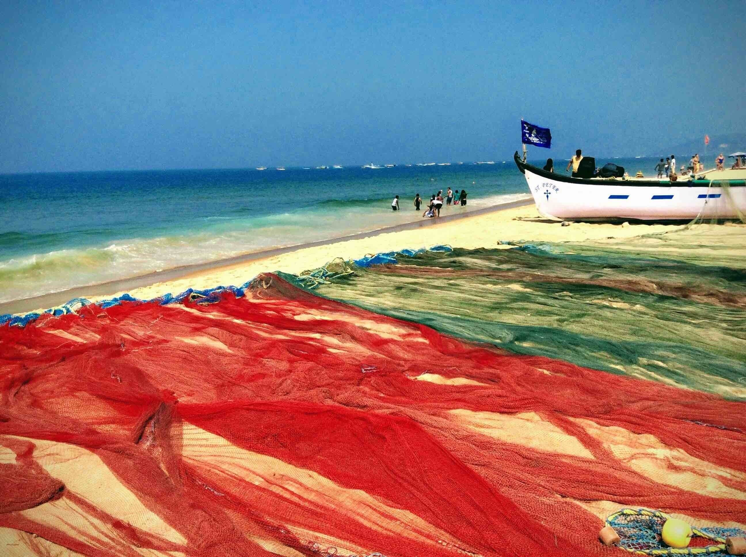 A beach with a boat, people, and a colorful net.