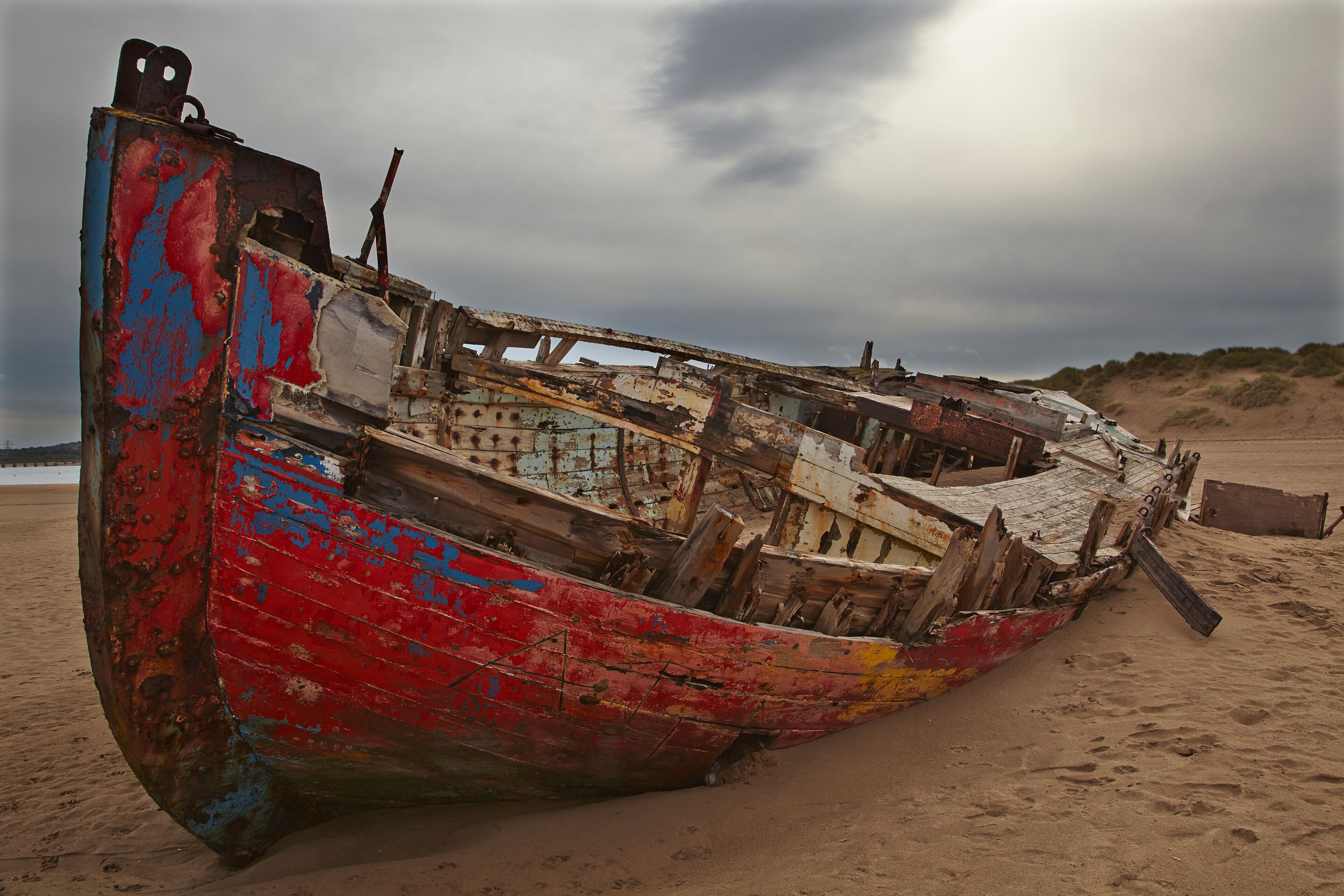 A weathered, colorful boat on a sandy beach with overcast skies.