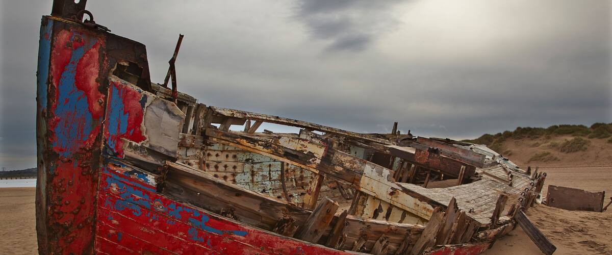 A weathered, colorful boat on a sandy beach with overcast skies.