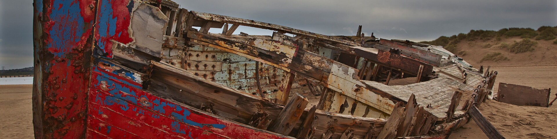 A weathered, colorful boat on a sandy beach with overcast skies.
