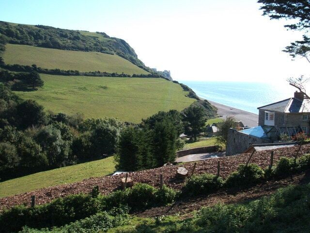 A coastal landscape with a stone house, green fields, and a beach.