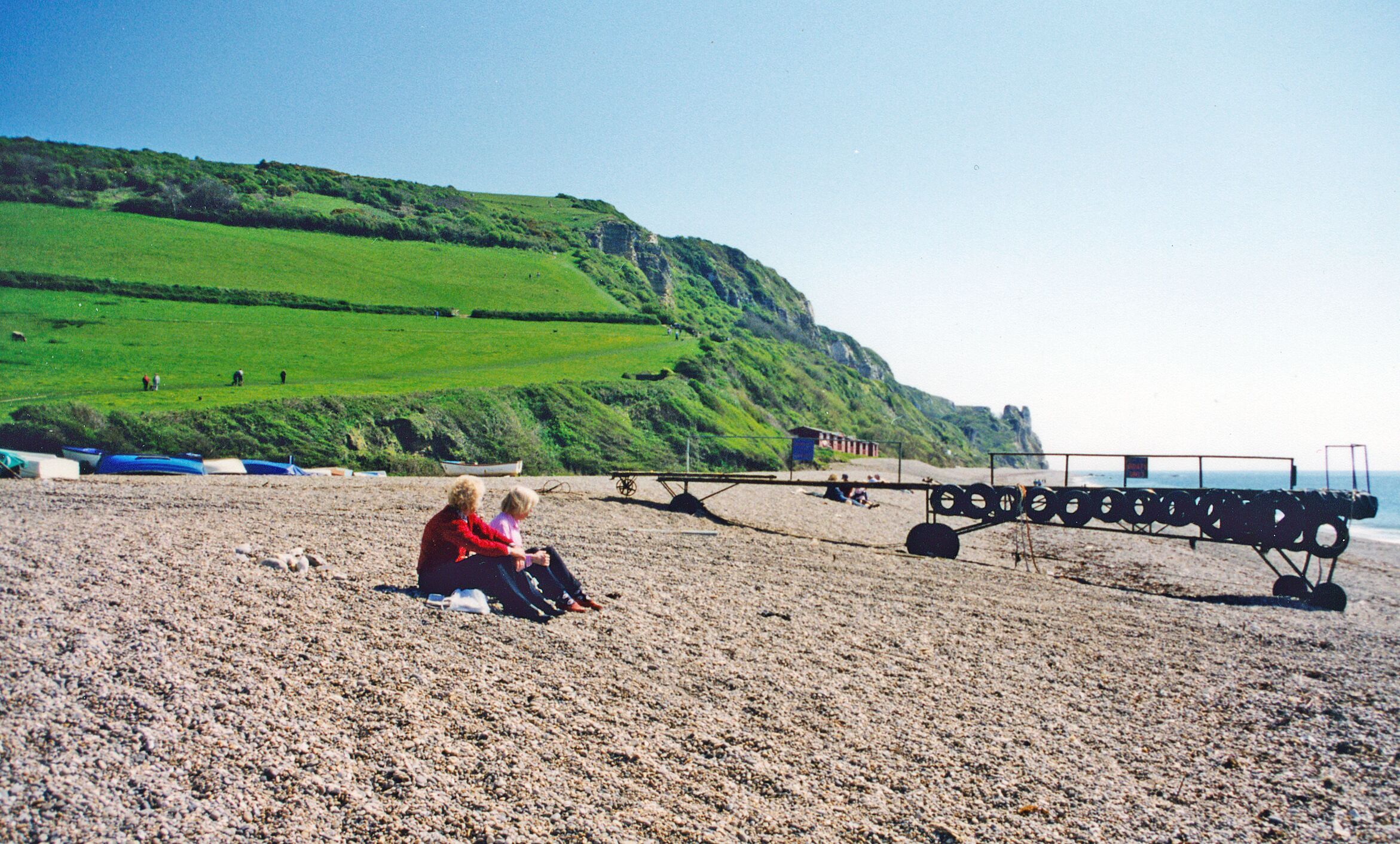 A beach with a grassy hill in the background, a swing set, and a few people.