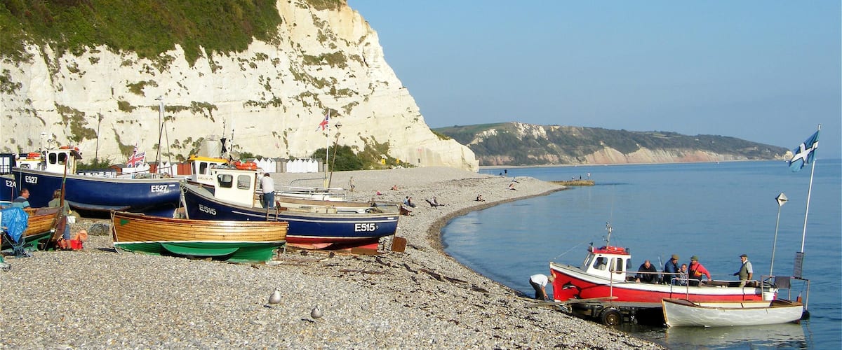 A rocky beach with several boats, cliffs, and a clear blue sky.