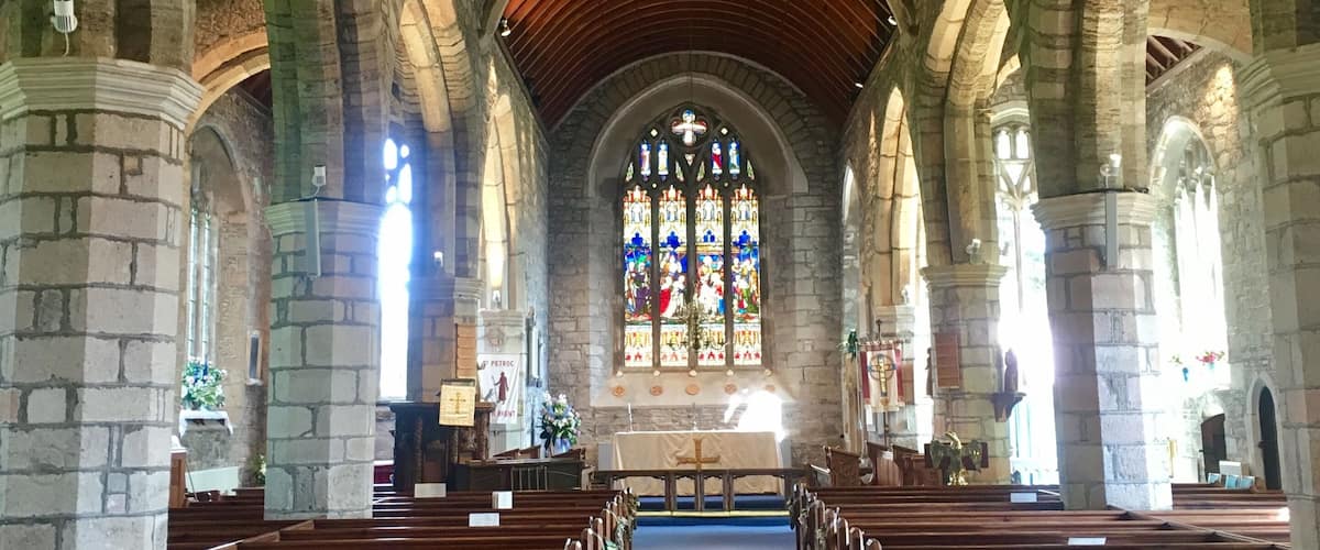 An interior of a church with stone arches, wooden pews, and a stained glass window.
