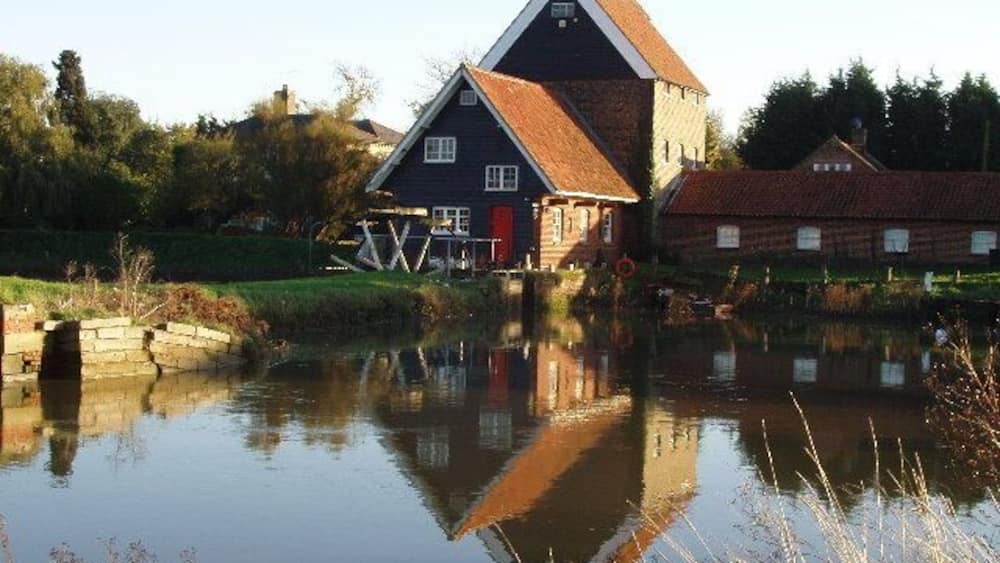 A traditional house by a calm river with a wooden bridge and a stone wall.