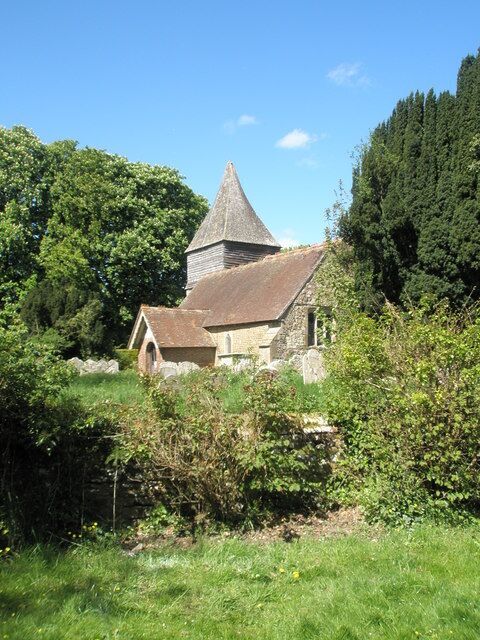 A stone church with a conical roof surrounded by greenery.