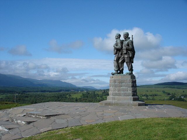 A statue of two figures on a stone pedestal with a scenic landscape in the background.