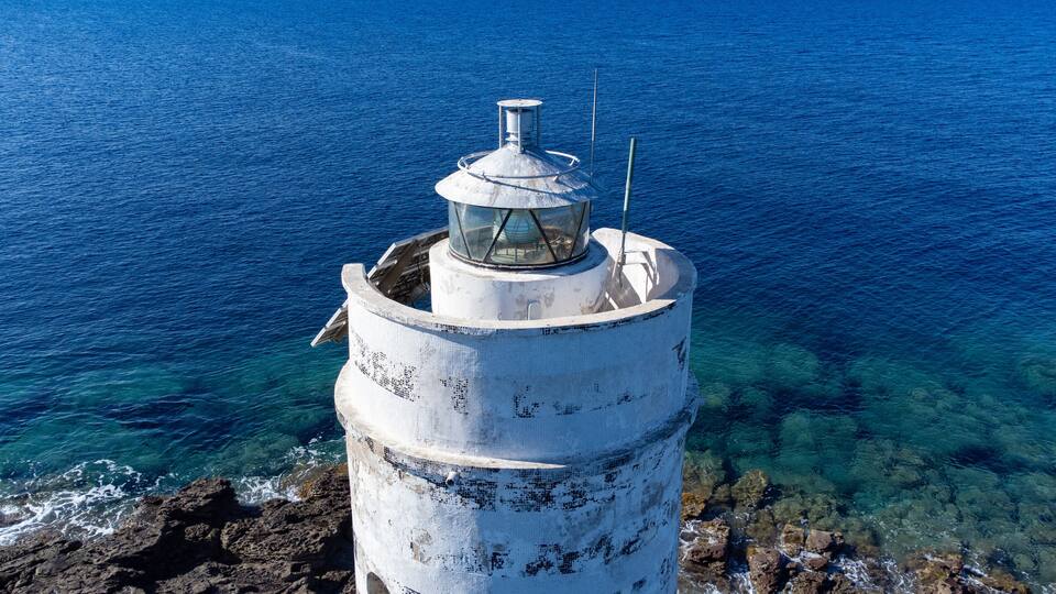 A lighthouse on a rocky coastline with clear blue waters.