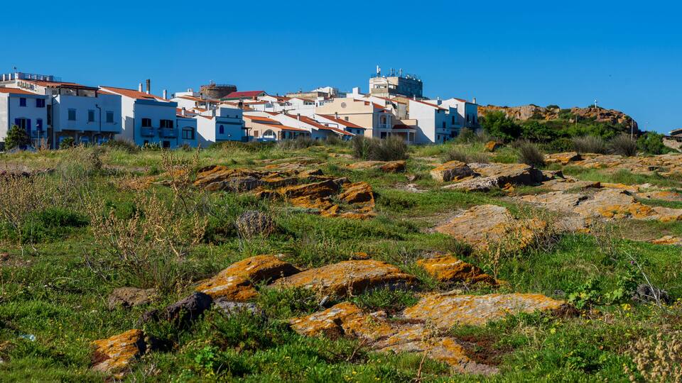 A coastal village with white buildings, rocky terrain, and sparse vegetation.