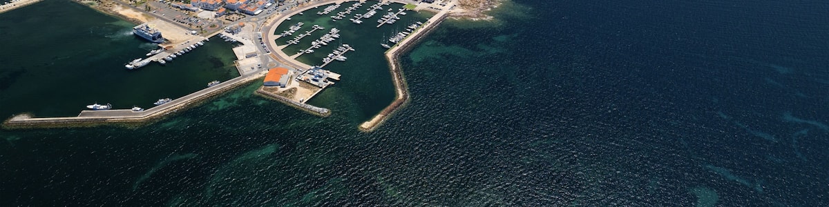 An aerial view of a coastal town with a marina, dense housing, and surrounding water bodies.