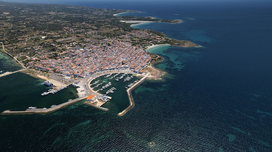 Aerial view of the harbor filled with boats contrasting against the backdrop of the town's red-tiled roofs and the deep blue sea, Calasetta, Sardinia, Italy.