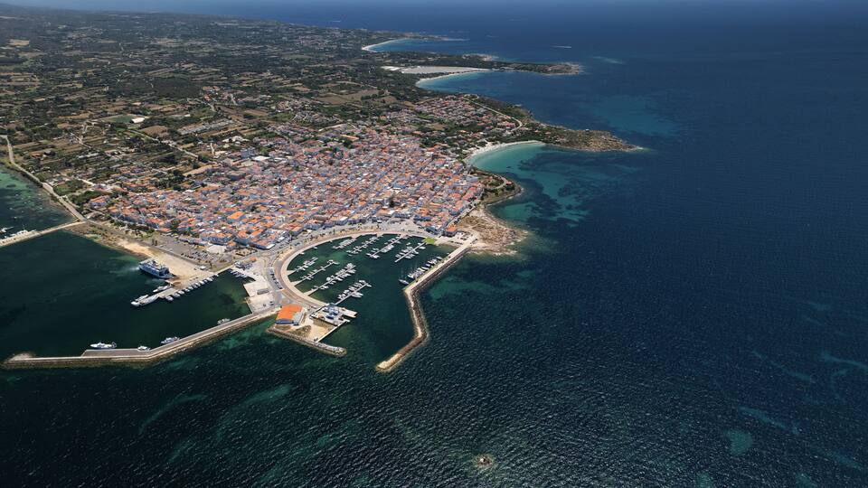 An aerial view of a coastal town with a marina, dense housing, and surrounding water bodies.