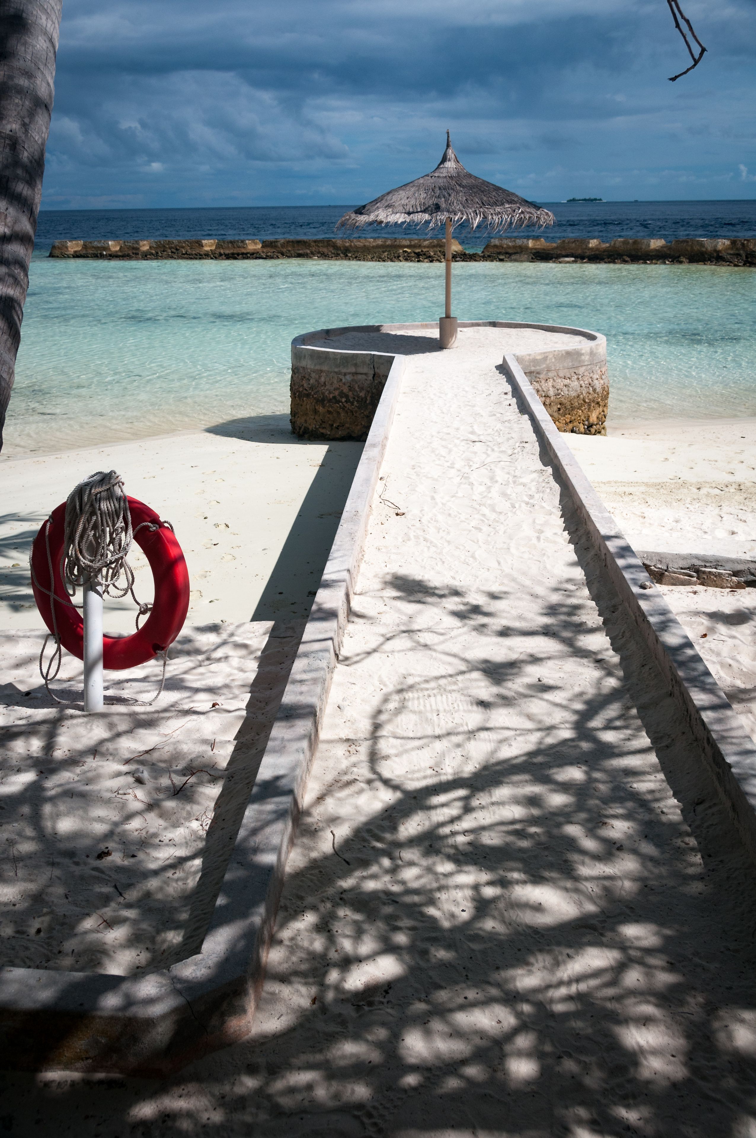 En strandsti der fører hen til en bindingsværksbygning, en redningskrans og en palme.