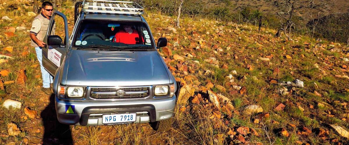 A silver Toyota with a roof rack parked on a rocky hillside.