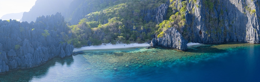 A coastal landscape with clear turquoise waters, rocky cliffs, and a sandy beach.