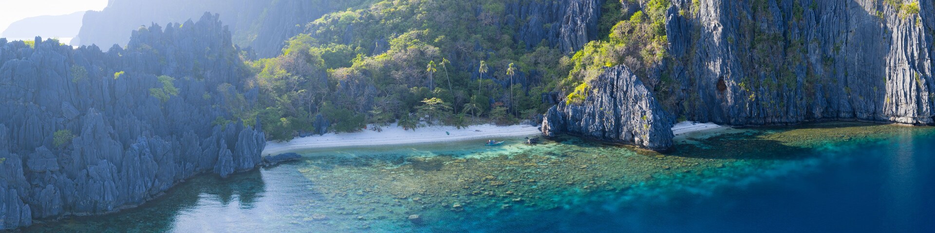 Paisagem costeira com águas turquesa cristalinas, falésias rochosas e uma praia arenosa.