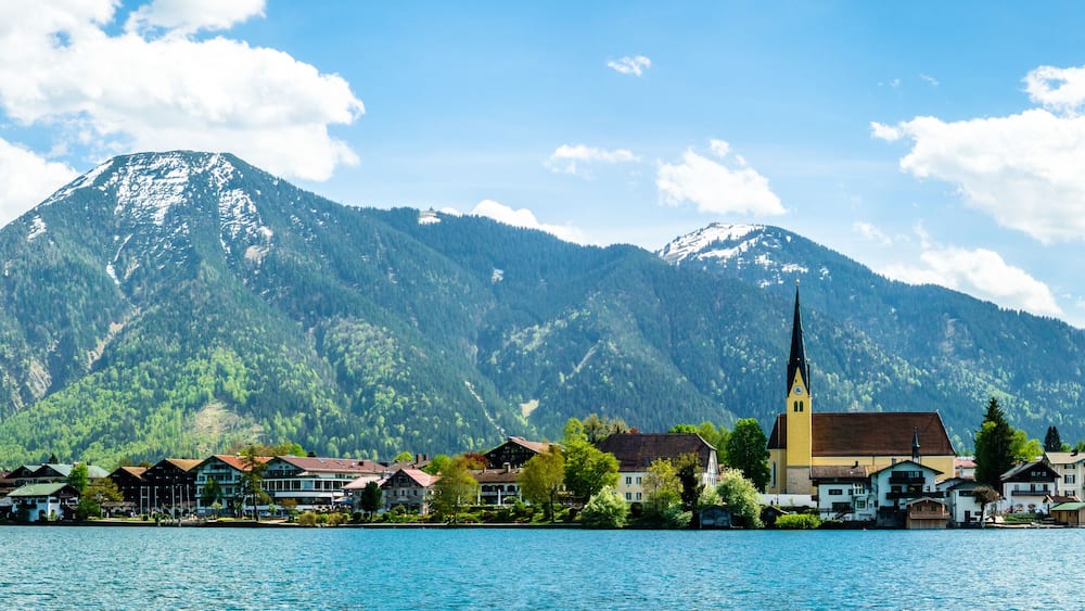 A lakeside town with a church and mountains in the background.