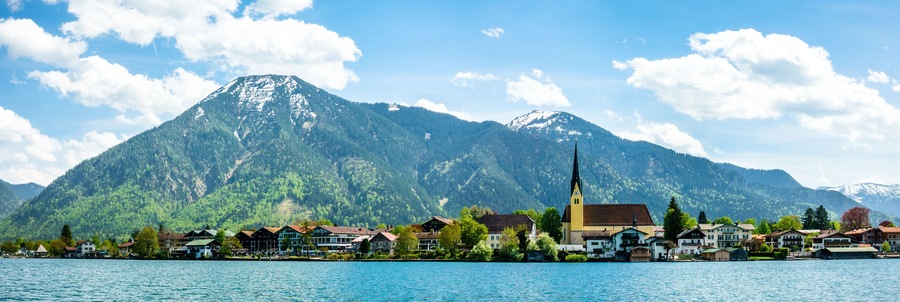 A lakeside town with a church and mountains in the background.