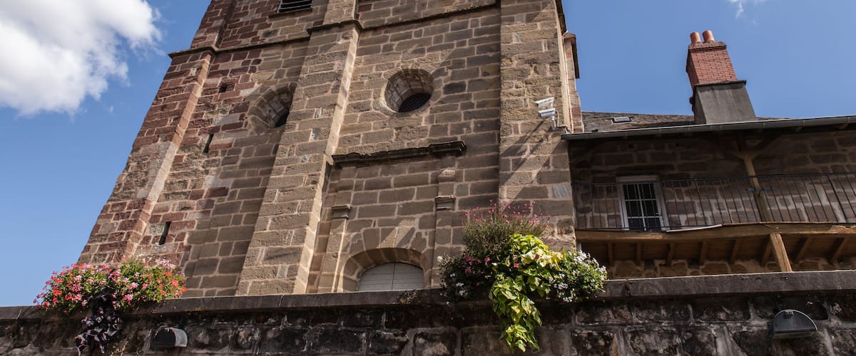 A historic stone tower with arched windows and a bell tower, surrounded by flowering plants.