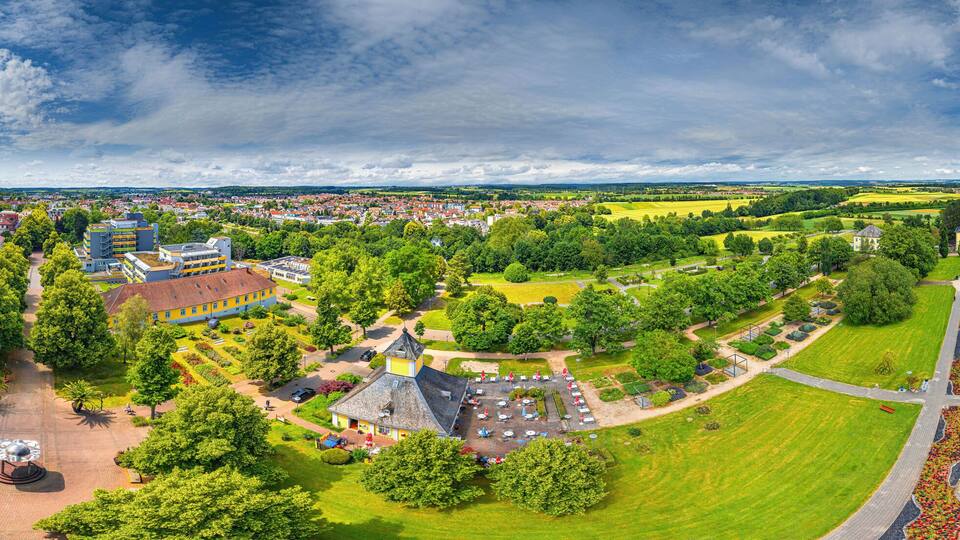 A panoramic view of a town with a central park, a large circular monument, and surrounding buildings.