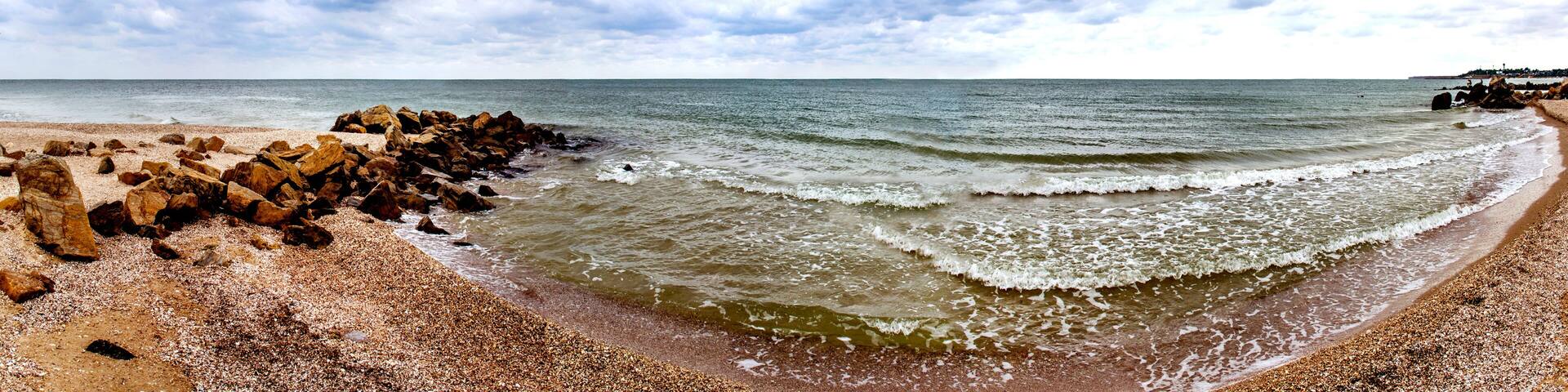 A rocky beach with waves, a clear sky, and distant land.