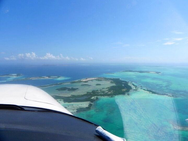 An aerial view of a turquoise sea with clear waters and a white aircraft wing.