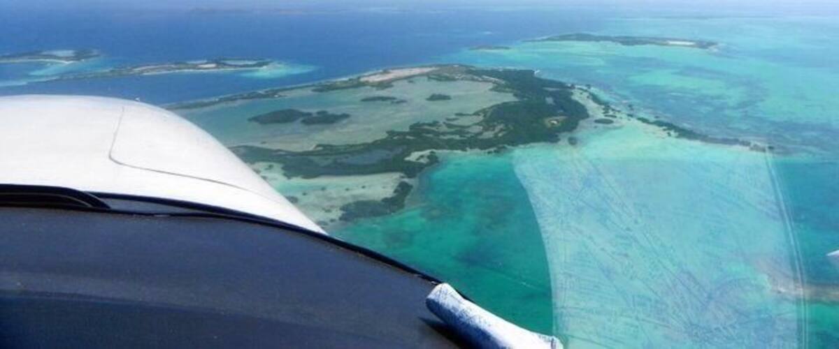 An aerial view of a turquoise sea with clear waters and a white aircraft wing.