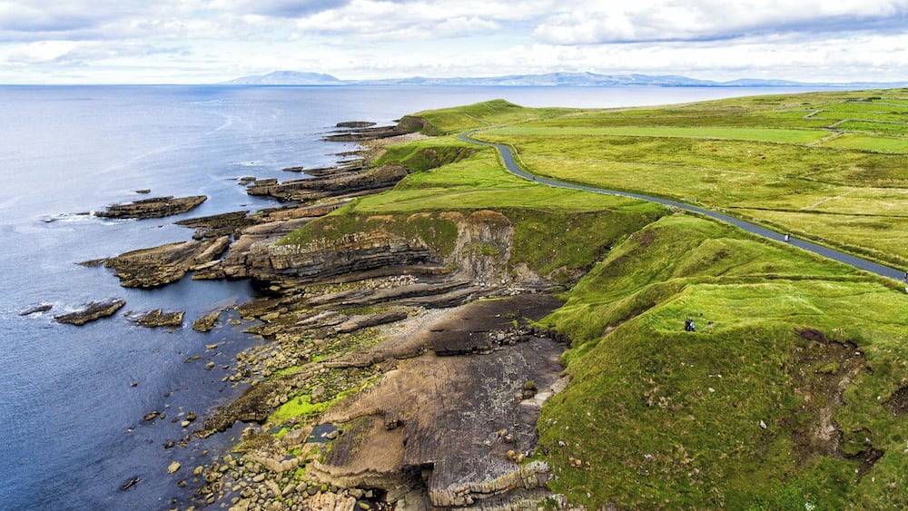 A coastal landscape with cliffs, a winding road, and distant mountains.