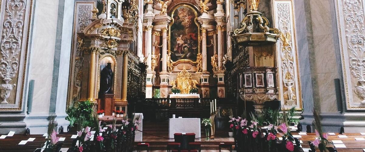 An ornate church interior with a checkered floor, rows of pews, and elaborate ceiling frescoes.