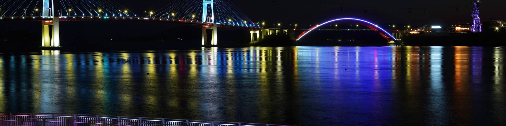 A nighttime view of a cable-stayed bridge with illuminated cables and a lit arch.