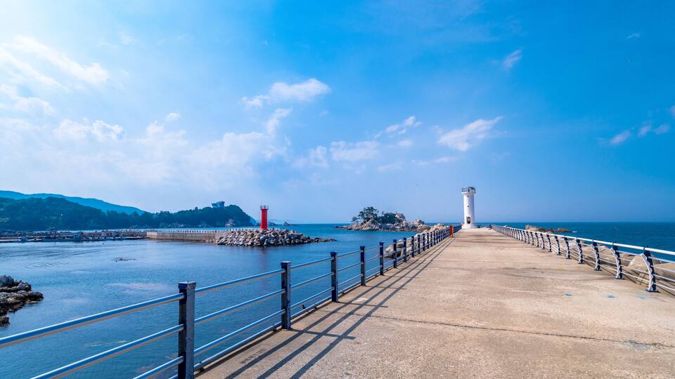 A coastal walkway with a lighthouse and rocky outcrops.