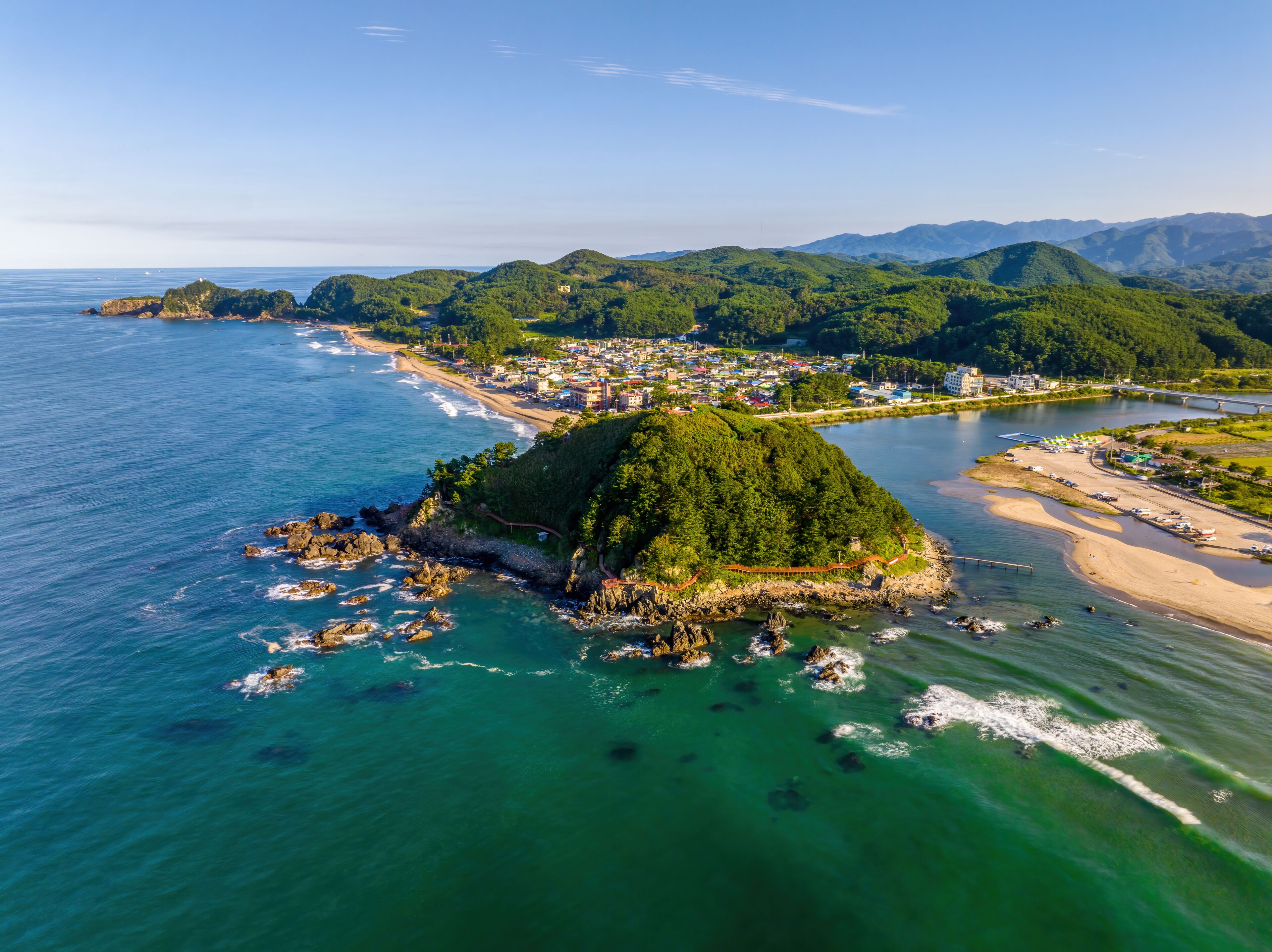 Summer and afternoon view of sea wave on seaside rock and Deokbongsan Mountain against Maeupcheon Stream and villages at Deoksan-ri near Samcheok-si, South Korea
