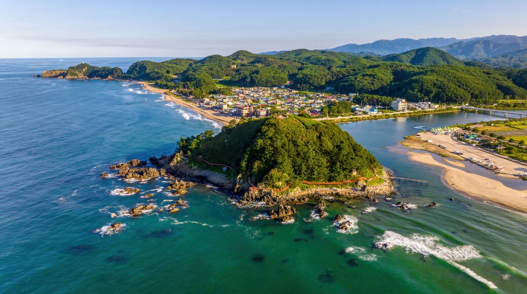 Summer and afternoon view of sea wave on seaside rock and Deokbongsan Mountain against Maeupcheon Stream and villages at Deoksan-ri near Samcheok-si, South Korea