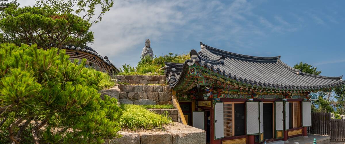 A traditional Korean temple with ornate architecture, a stone pathway, and a statue in the background.