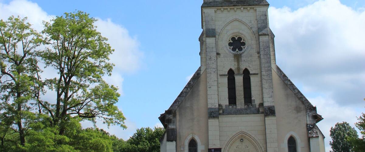 A church with a tall spire and a cross at the top, surrounded by greenery and trees.