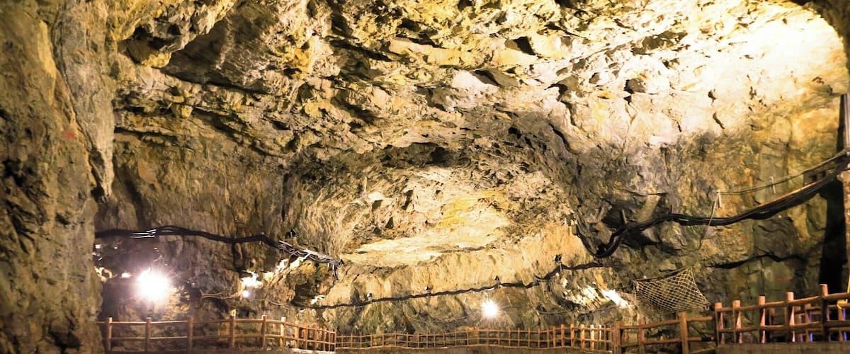 A cave with a wooden walkway over water, illuminated by lights.