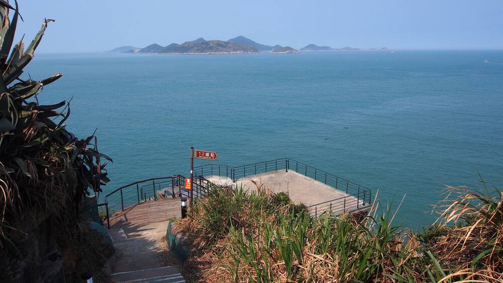 A coastal staircase leading to a viewing platform with a sign indicating the distance to the sea.