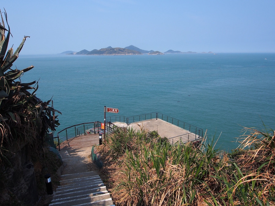 Eine Küstenstiege führt zu einer Aussichtsplattform, auf der die Entfernung zum Meer ausgeschildert ist.