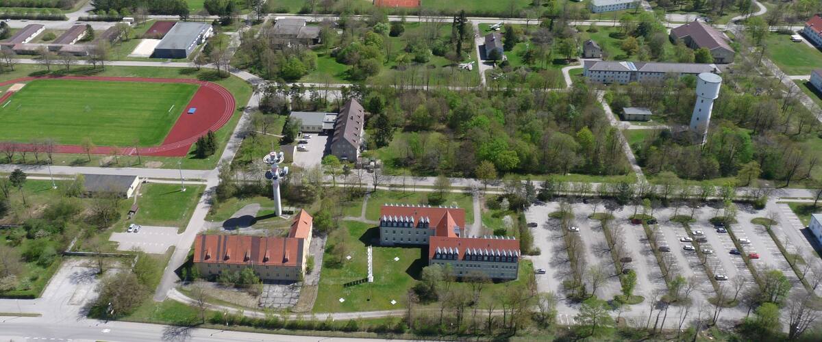 An aerial view of a campus with a large sports field, multiple buildings, and a parking lot.